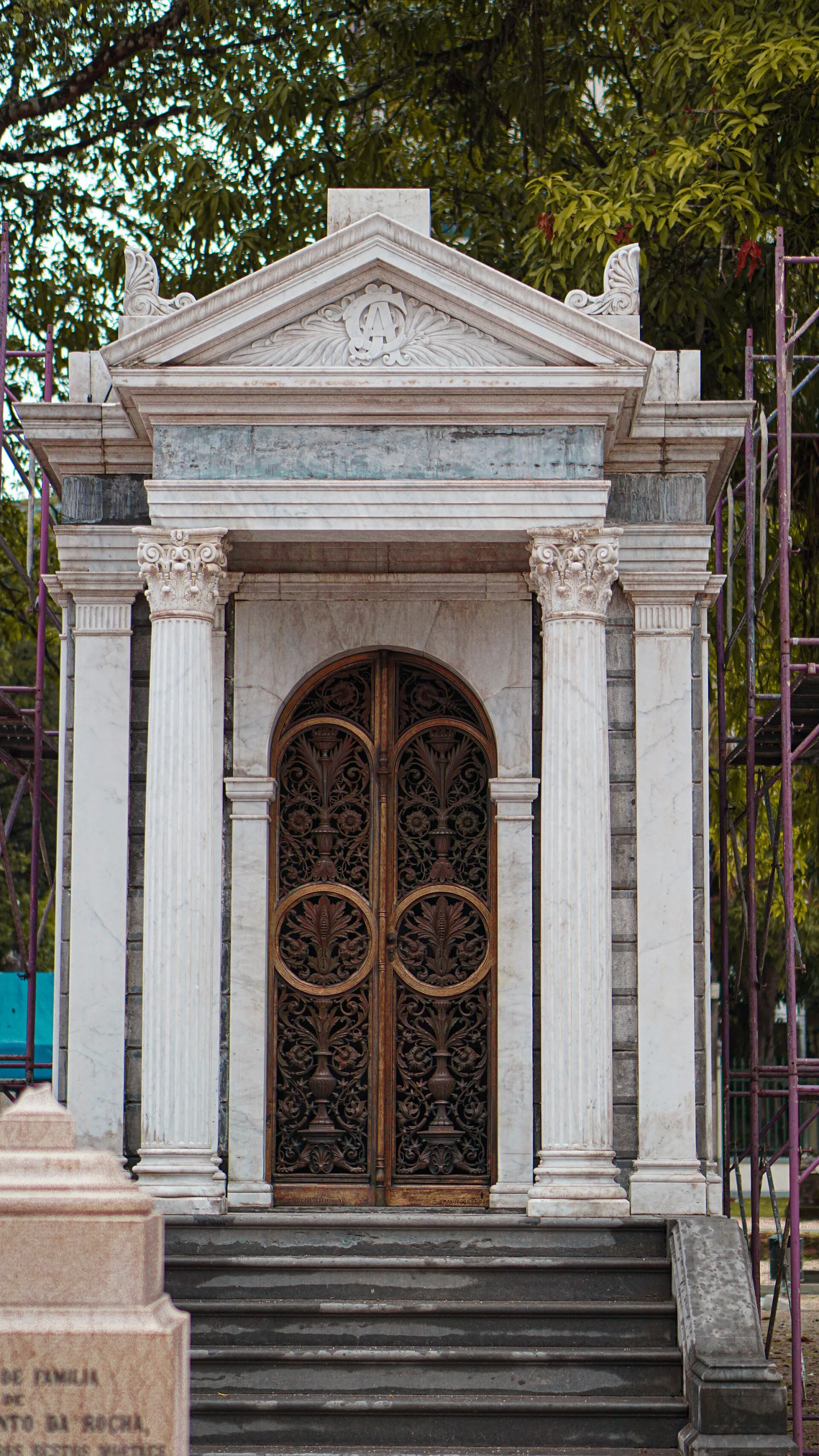 Panteón de mármol blanco con columnas y frontón clásico y una puerta de hierro labrado en el cementerio de La Soledad de Huelva