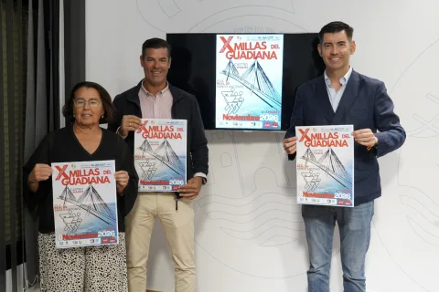 Tres personas de pie sostienen carteles de la carrera X Millas del Guadiana ante una pantalla con el mismo cartel.
