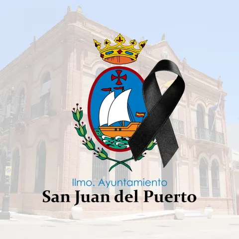 Escudo municipal con corona, velero y lazo negro sobre la fachada de un edificio de ladrillo y el texto Ilmo. Ayuntamiento San Juan del Puerto.